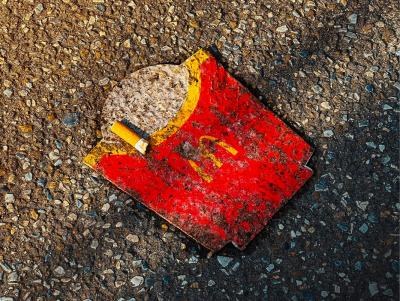 Photo of an empty McDonalds chip carton with a cigarette butt on top, lying on the ground